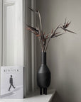A 101 Copenhagen Duck Slim Coffee 111280 vase sits next to a book on a window sill.