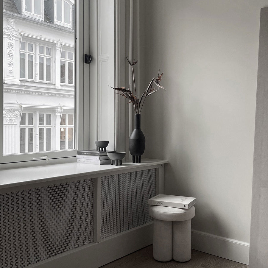 A 101Cph Duck Slim Coffee 111280 ceramic stool placed in front of a window in Copenhagen.