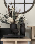 A 101Cph Duck Slim Coffee 111280 vase from 101 Copenhagen sits on a table in front of a round mirror.