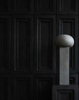 An architectural reference of a ceramic 101Cph Empire Big Dark Grey 223034 vase, resembling a concrete ball, elegantly sits on a pedestal in front of a black wall.
