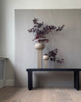 A table with two quirky vases, 101 Copenhagen Empire Mini Sand 223037, and a painting on the wall.