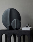 A table with two 101Cph Guggenheim Petit Black 213042 spheres and a book on it showcasing quirky vases.