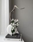 A quirky 101Cph Guggenheim Petit Bone White 213043 vase with flowers sitting on a window sill.