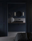 Modern bathroom with dark blue walls, round mirror, and sculptural vase from 101 Copenhagen