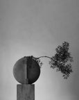 A sculptural vase with a branch against a gray background from 101 Copenhagen at Spacio retail stores in Mumbai & Kolkata.