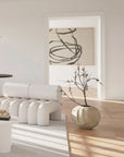 Modern interior with white furniture, a vase with branches, and abstract art on a light-colored wall.