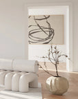 Modern interior with white furniture, a vase with branches, and abstract art on a light-colored wall.