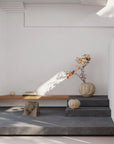 Modern interior with a white wall, wooden bench, stone stools, and decorative items.