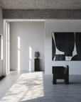 Modern interior with a black chair, abstract painting, and concrete wall and a pedestal with vase from 101 Copenhagen