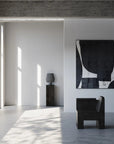 Modern interior with a black chair, abstract painting, and concrete wall and a pedestal with vase from 101 Copenhagen