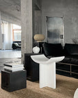 Modern interior with a black sofa, white table, and concrete walls.