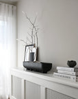 Decorative setup with black bowl, branches, and books on a white surface.