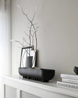 Decorative setup with black bowl, branches, and books on a white surface.