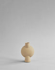 A beige vase with a sand finish sitting on a gray surface. This Scandinavian brand, 101 Copenhagen, offers the stylish 101Cph Sphere Bubl Mini Sand 203008 as an elegant home decor piece.