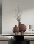 A living room with two 101Cph Sphere Bubl Mini Terracotta 203010 vases by 101 Copenhagen on a table.