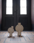 Two 101Copenhagen Sphere Vase Bubl Big Sand 201014 vases from 101 Copenhagen are elegantly placed on a tile floor in an empty room.