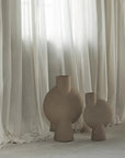 Two 101Cph Sphere Vases with a Sand finish sitting next to each other in front of a curtain.