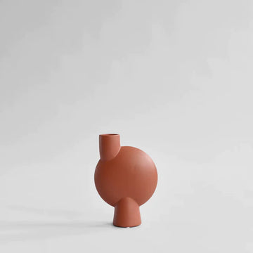 A small red 101Cph Sphere Vase Bubl Medio Cinnamon 221035 (Limited Edition) by 101 Copenhagen, with a cinnamon finish, sitting on a white surface.