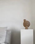Decorative vase on a white pedestal against a plain wall with gray cushions from 101 Copenhagen at Spacio retail stores in Mumbai & Kolkata.