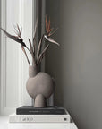 Gray vase with dried plants on books against a gray wall from 101 Copenhagen at Spacio retail stores in Mumbai & Kolkata.
