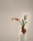 Terracotta ceramic sculptural vase with orange flowers on a white pedestal against a plain background from 101 Copenhagen at Spacio retail stores in Mumbai & Kolkata.