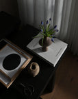 Vase with flowers on a book on a dark surface with a curtain in the background