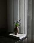 Sculptural Vase with flowers on a book against a curtain backdrop from 101 Copenhagen at Spacio retail stores in Mumbai & Kolkata.