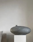 Decorative vase on a pedestal against a plain wall with a pillow partially visible from 101 Copenhagen at Spacio retail stores in Mumbai & Kolkata.