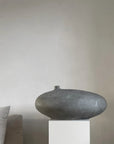 Decorative vase on a pedestal against a plain wall with a pillow partially visible from 101 Copenhagen at Spacio retail stores in Mumbai & Kolkata.