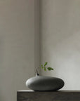Dark gray vase with a small plant on a neutral background from 101 Copenhagen at Spacio retail stores in Mumbai & Kolkata.