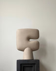 Beige abstract sculptural vase on a black base against a plain background from 101 Copenhagen at Spacio retail stores in Mumbai & Kolkata.