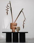 A pair of hollow sculptures on a black platform with dried plants against a white background from 101 Copenhagen at Spacio retail stores in Mumbai & Kolkata.