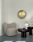 Modern interior with a textured armchair, round table, and abstract sculpture against a white wall.