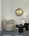 Modern interior with a textured armchair, round table, and abstract sculpture against a white wall.