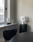 Modern interior with white sculptural vases on a windowsill and plinth (pedestal) and black chair.