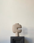 Beige abstract sculpture on a dark pedestal (plinth) against a plain wall from 101 Copenhagen at Spacio retail stores in Mumbai & Kolkata.