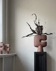 Two sculptures from the Tribal Collection, displayed on a table in front of a window. The sculptures, including the 101Cph Tribal Vase Medio Terracotta 214004, showcase stunning terracotta colors. The sculptures, including the 101Cph Tribal Vase Medio Terracotta 214004, showcase stunning terracotta colors.