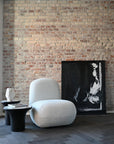 Modern living room with a textured brick wall, white armchair, and abstract painting.