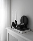 Decorative setup with black vases, candles, and a book on a white surface.