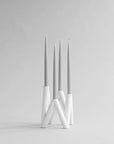 White candle holder with three candles on a light gray background from 101 Copenhagen at Spacio retail stores in Mumbai & Kolkata.