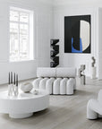 Modern living room with white furniture, abstract art, and a round coffee table.