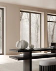 Modern interior with a black dining table and white chairs, large windows showing trees outside.