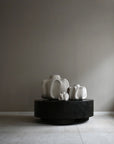 Three white ceramic sculptures on a black round platform against a plain wall from 101 Copenhagen at Spacio retail stores in Mumbai & Kolkata.