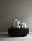 Three white ceramic sculptures on a black round platform against a plain wall from 101 Copenhagen at Spacio retail stores in Mumbai & Kolkata.