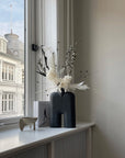 Decorative vase with flowers on a windowsill with a view of a building outside.