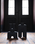 Two black vases from 101 Copenhagen in a dimly lit room with large windows.
