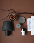 Decorative items including a black vase, gray containers, a bowl of nuts, and a magazine on a brown surface from 101 Copenhagen at Spacio retail stores in Mumbai & Kolkata.