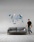 Man standing next to a gray sofa with a world map wall decal in a room.