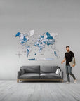 Man standing next to a gray sofa with a world map wall decoration in a room.
