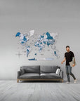 Man standing next to a gray sofa with a world map wall decoration in a room.